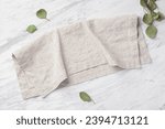 Natural linen napkin folded on marble kitchen table with green leaves, top view