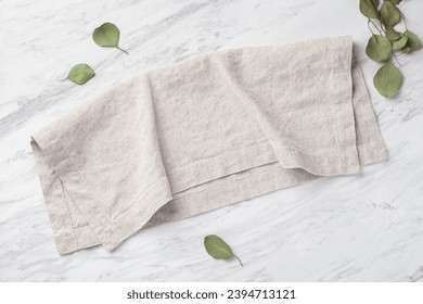 Natural linen napkin folded on marble kitchen table with green leaves, top view