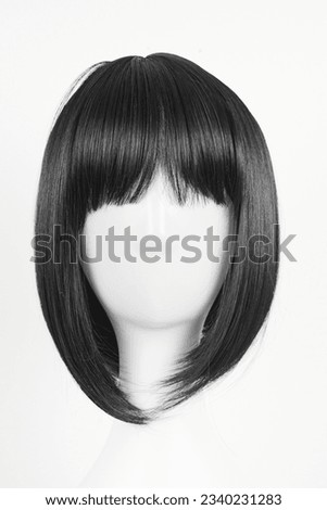 Natural looking black wig on white mannequin head. Medium length straight hair with bangs on the metal wig holder isolated on white background, front view