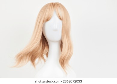 Natural looking blonde fair wig on white mannequin head. Middle length hair cut on the plastic wig holder isolated on white background, front view
