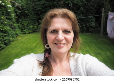 natural looking mature woman taking a selfie in back garden 