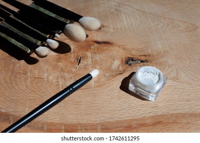 Natural makeup brushes on a green pottery holder. Wooden background of slab from exotic wood. Silver sparkles in a plastic jar.  - Powered by Shutterstock