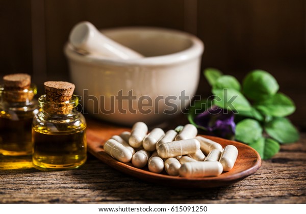 Natural medicine capsule pill with herb,\
essential oil and ceramic mortar on wooden background for\
alternative medical\
concept.