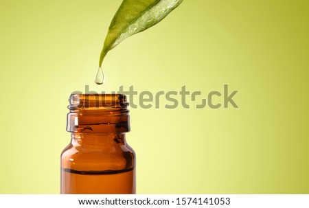 Natural medicine concept with leaf and drop falling into glass jar with medicinal liquid and green gradient background. Horizontal composition. Front view.