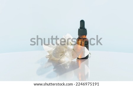 Natural medicine or essential aroma oil or beauty essence amber glass vial with dropper with white flowers and airy blue background. Face and body spa serum care concept banner