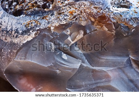 Natural mineral stone - brown flint stone. The texture of chipped flint close-up. Traces of chips on the surface of flint stone.