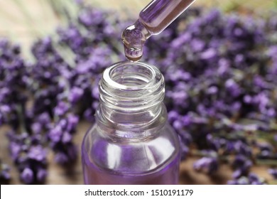 Natural Oil Dripping Into Bottle And Lavender Flowers On Table, Closeup. Cosmetic Product