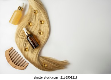 A natural oil or serum for hair care and a ply of blonde hair lying on a white background - Shutterstock ID 2168501219