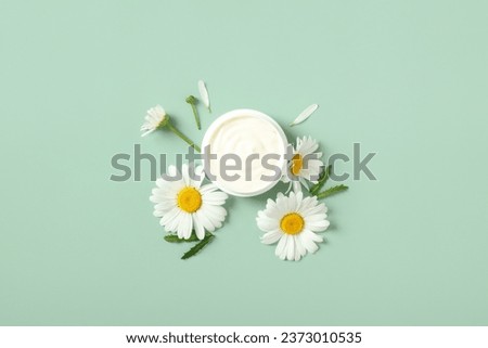 Natural organic moisturizer cream with chamomile buds on green background. Flat lay, top view.