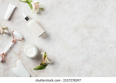 Natural Organic SPA Beauty Products On Stone Table. Flat Lay Face Massage Roller, Serum, Moisturizer Cream, Flowers. Skin Care And Treatment Concept.