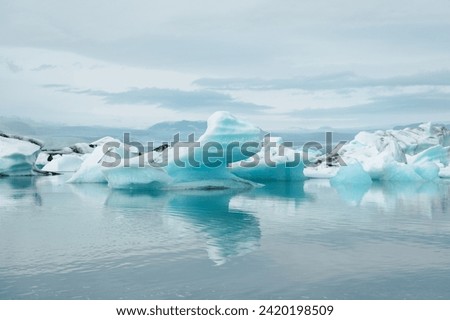 Natural outdoor Jokulsarlon glacial lake with calm cold blue water, unique floating icebergs, snowy mountain, cloudy gray sky 
