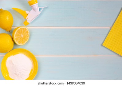 Natural Products For Eco Friendly Cleaning. Lemon, Baking Soda And Vinegar For Eco Housekeeping. All Objects, Lemon, Bowl, Washing Sponge, Pump Sprayer  Are In Yellow Color. Blue Wooden Background.