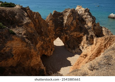 Natural rock archway leading to hidden beach, bathed in sunlight and surrounded by vibrant ocean blues. - Powered by Shutterstock