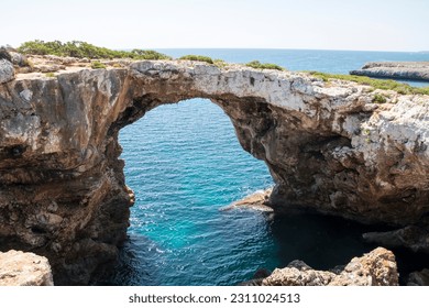 Natural rock bridge on the coast of mallorca with bright blue transparent sea. Warm sunny summer day. - Shutterstock ID 2311024513