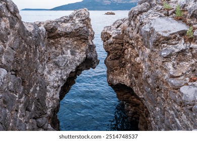 A natural rock crevice opens up to the calm blue water, creating a striking contrast between the rugged rocks and serene sea. - Powered by Shutterstock