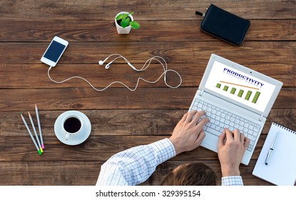 Natural Rough Wooden Desk And Man Working On Computer Top View Smart Casual Clothing Typing On Keyboard With Productivity Chart On Screen Smart Phone And Cup Of Coffee Aside