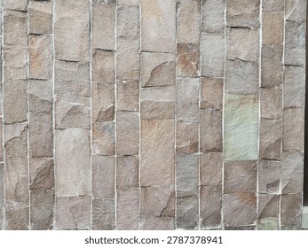 Natural sandstone wall cladding in vertical linear pattern. Earthy mix of brown, taupe, and grey tones with subtle hints of rust red and green. Each stone has a unique rough, cleft surface with natural chips and variations. The clean white grout lines create strong vertical rhythm, adding structure to the organic texture.