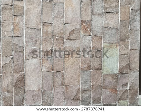 Natural sandstone wall cladding in vertical linear pattern. Earthy mix of brown, taupe, and grey tones with subtle hints of rust red and green. Each stone has a unique rough, cleft surface with natural chips and variations. The clean white grout lines create strong vertical rhythm, adding structure to the organic texture.