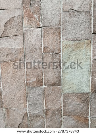 Natural sandstone wall cladding in vertical linear pattern. Earthy mix of brown, taupe, and grey tones with subtle hints of rust red and green. Each stone has a unique rough, cleft surface with natural chips and variations. The clean white grout lines create strong vertical rhythm, adding structure to the organic texture.