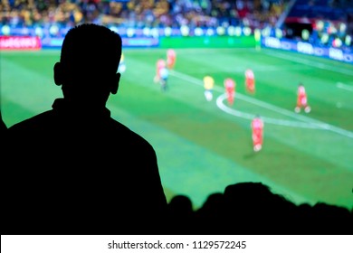 Natural silhouetes of  young football fans crowd spectators watching soccer match on big screen on city square