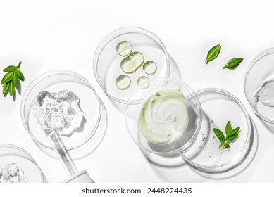 Natural skin care products swatches in petri dish with dropper and green plants isolated on white background. Trendy beauty product with hard shadows, organic vegan plant based skin care concept.