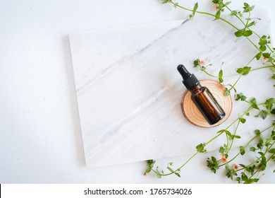 Natural Skincare Serum In Dropper Bottle On Marble Background With Flower, Leaf And Pestle Mortar . Cosmetic Beauty Background.