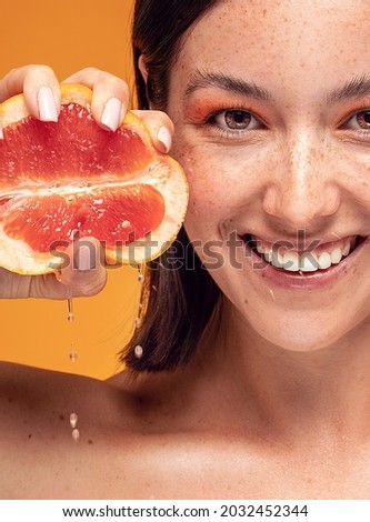 Natural smiling girl with fresh grapefruit. Beauty model squeezing juicy fruit. Joyful woman with natural freckles on face. Concept of a healthy skin care, cosmetology. 
