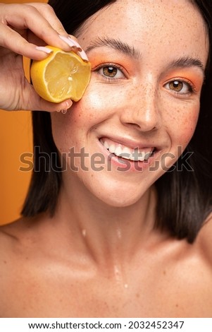 Natural smiling girl with fresh lemon. Beauty model squeezing juicy fruit. Joyful woman with natural freckles on face. Concept of a healthy skin care, cosmetology. 
