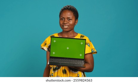 Natural smiling woman posing with a green screen on laptop, making an advertisement with isolated mockup display in studio. Young traditional person in tribal native clothing. Camera A. - Powered by Shutterstock