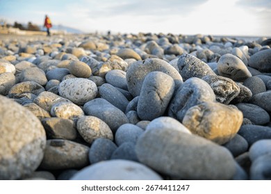 Natural smooth pebbles in sharp focus on rocky beach close up with soft sky and blurred people in background by the black sea.