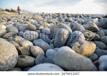 Natural smooth pebbles in sharp focus on rocky beach close up with soft sky and blurred people in background by the black sea.