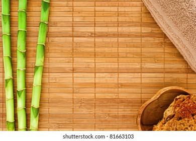 Natural spa background framed by green bamboo stems over brown mat with cotton towel and natural bath sponge in a wood bowl in corners