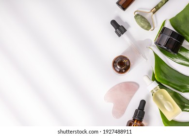 Natural SPA cosmetic products background, Composition with bottles of essential oils, cream, massage rollers and tropical leaf on white background - Shutterstock ID 1927488911