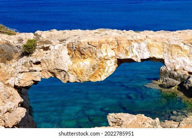 Natural stone arch Kamara Tou Koraka. Another name is Sinner Bridge. Cape Greco National Forest Park on the island of Cyprus. Azure water in the bay of the arch.
