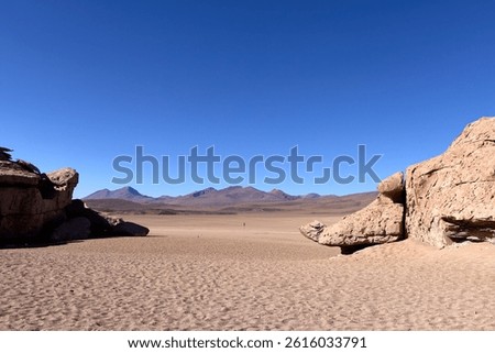 Natural stone gateway frames distant volcanic mountains across sandy desert plain in Eduardo Avaroa National Park, Bolivia. Dramatic rock formations under deep blue sky.