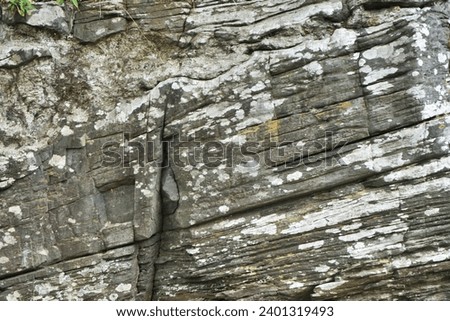Natural stone horizontal background with diagonal cracks and striations and contrasting lichen patches