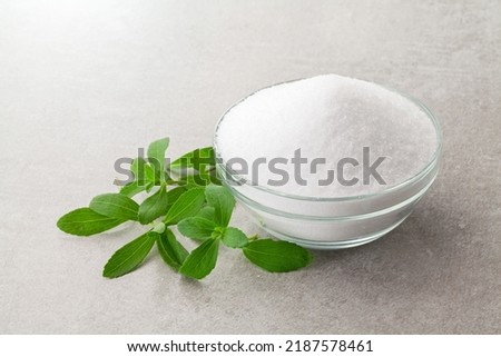 natural sugar substitute sweetener in a glass bowl with fresh stevia leaves.