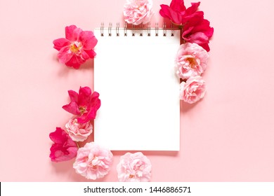 Natural template with blank notepad and various vintage roses on the pink background, top view