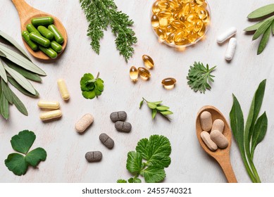 Natural vitamins, plant based supplements and green leaves flat lay on white wooden background. Various organic capsules and pills.