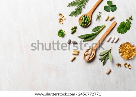 Natural vitamins, plant based supplements and green leaves on white wooden background, top view, copy space. Various organic capsules and pills.