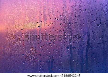 Natural water drops and sunlight on window glass, close-up purple background