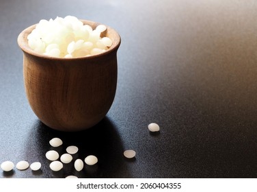 Natural White Beeswax Granules In A Wooden Cup. Black Background