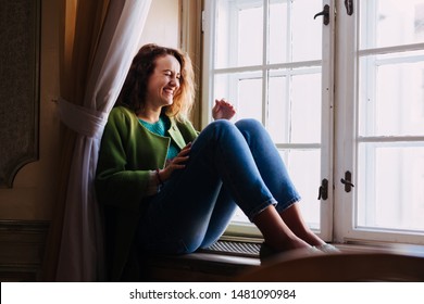 Natural woman laughing spontaneously  near a window. Warm dressed caucasian girl with curly hair. - Shutterstock ID 1481090984