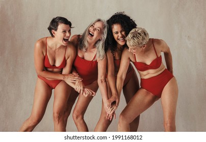Natural women of all ages celebrating their ageing bodies. Four happy and body positive women having fun while wearing red swimwear against a studio background.