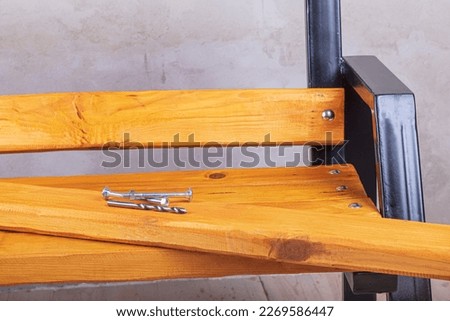 a natural yellow board is lying on a street bench. there are bolts and a drill located on it