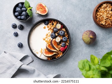 Natural yogurt with granola, berries and figs in a black bowl on a blue background with mint. Healthy and nutritious breakfast. Top view - Shutterstock ID 2216575111