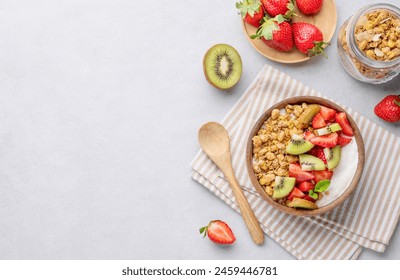 Natural yogurt with granola, kiwi and strawberries in a wooden bowl on a light background with fresh berries and fruits. Healthy and nutritious breakfast concept. Top view and copy space.