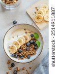 Natural yogurt with granola or muesli, banana and blueberries in a bowl on a white background with fresh berries in the morning light. Healthy and nutritious breakfast concept. Top view.