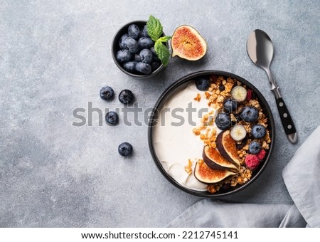 Natural yogurt with muesli, berries and figs in a black bowl on a blue background with napkin. Healthy and nutritious breakfast. Top view and copy spase.