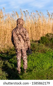 Naturalist Photographer In Action, With Camouflage And Camera, In The Wilderness. Seen From Behind With The Camouflage Suit.